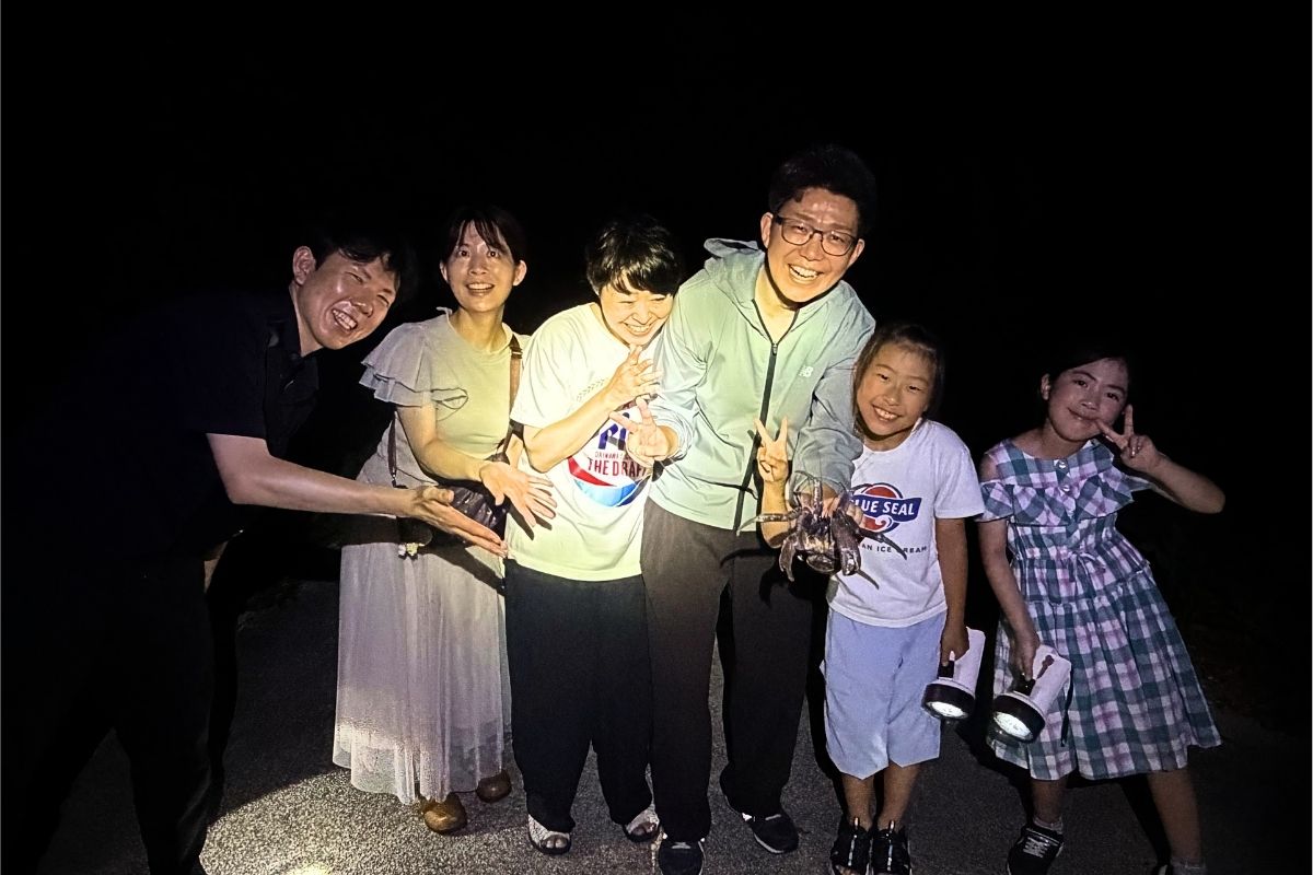 石垣島の星空ジャングルナイトツアーで捕まえたヤシガニと一緒に家族みんなで記念写真を撮影する様子 RUANOA
