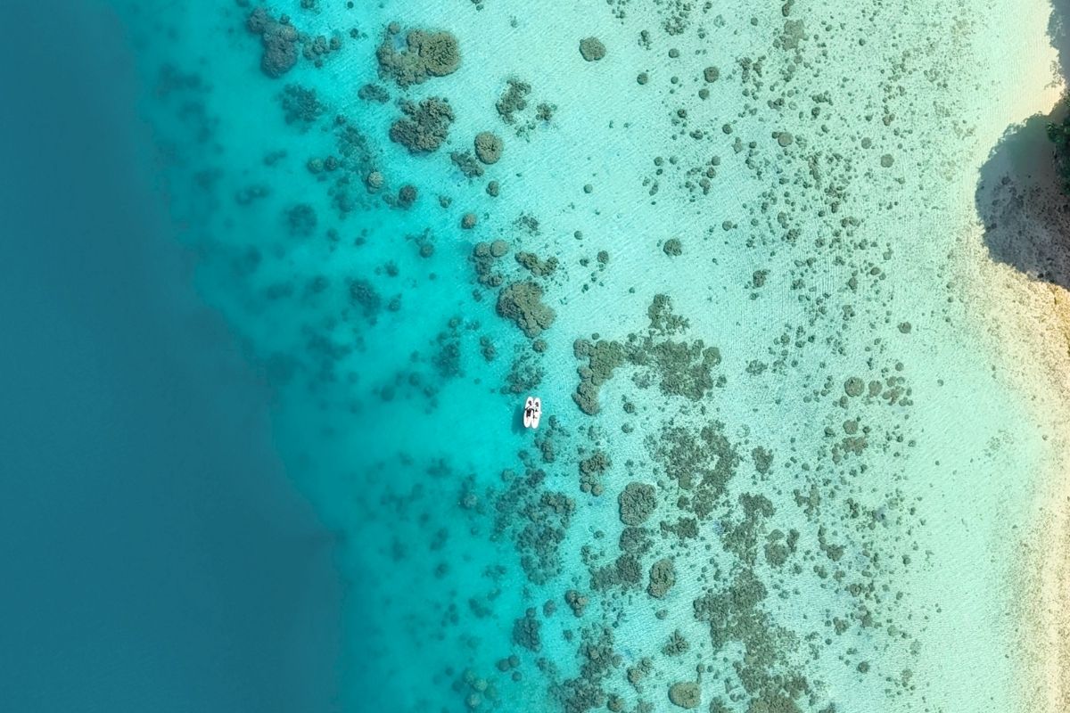 白い砂浜と透き通るサンゴ礁の境界線が美しい石垣島の海を、ドローンで広く見下ろしたSUP体験の絶景ロケーションフォト