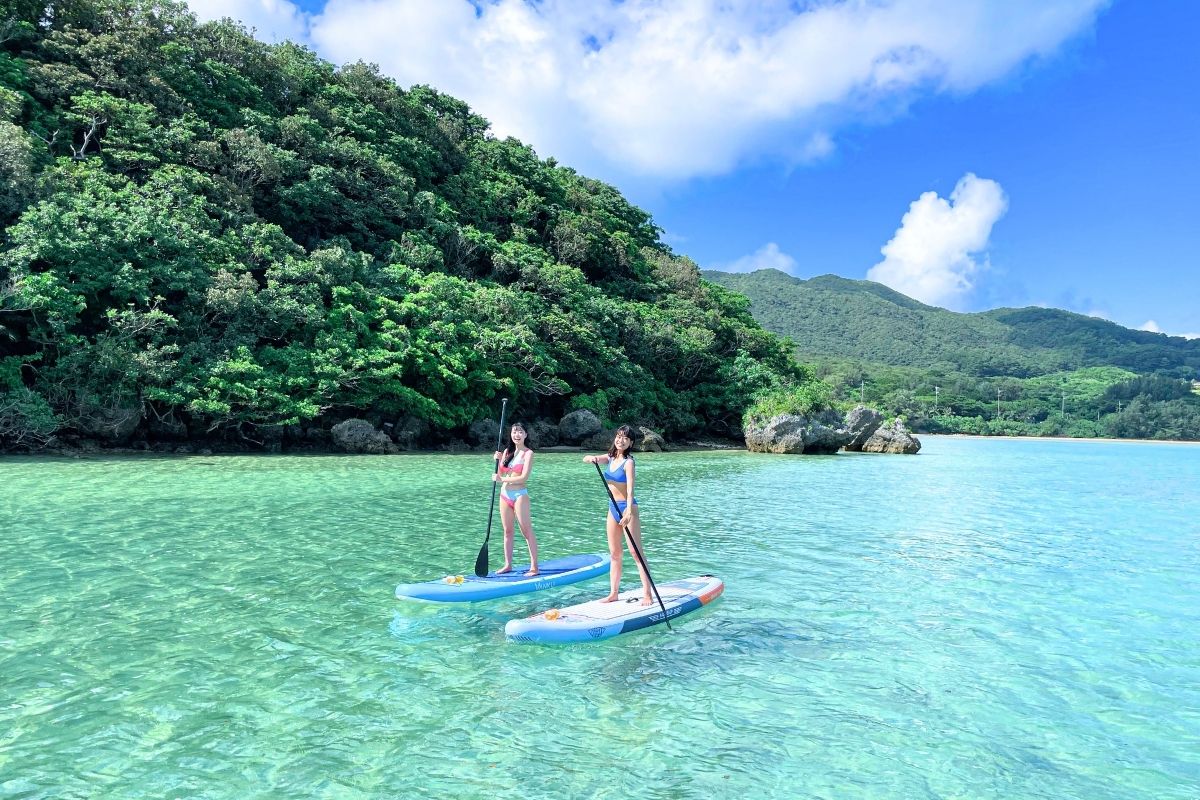 南国特有の鮮やかな緑に囲まれた石垣島の美しい海岸線に沿って、SUPクルージングをゆったり楽しむ女性たち