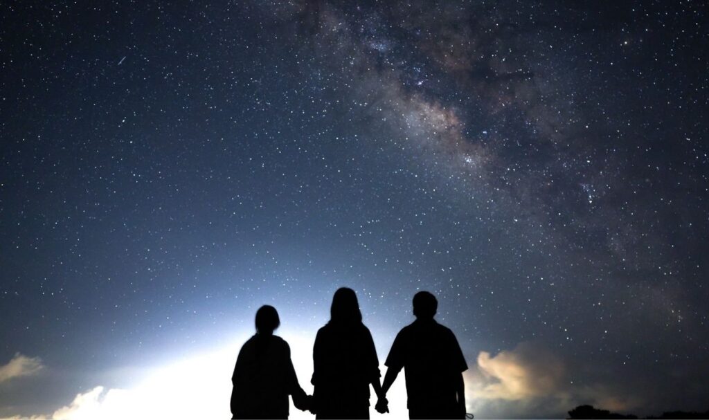 天然のプラネタリウムのような石垣島の星空の下で手を繋いで夜空を見つめる3人のシルエット