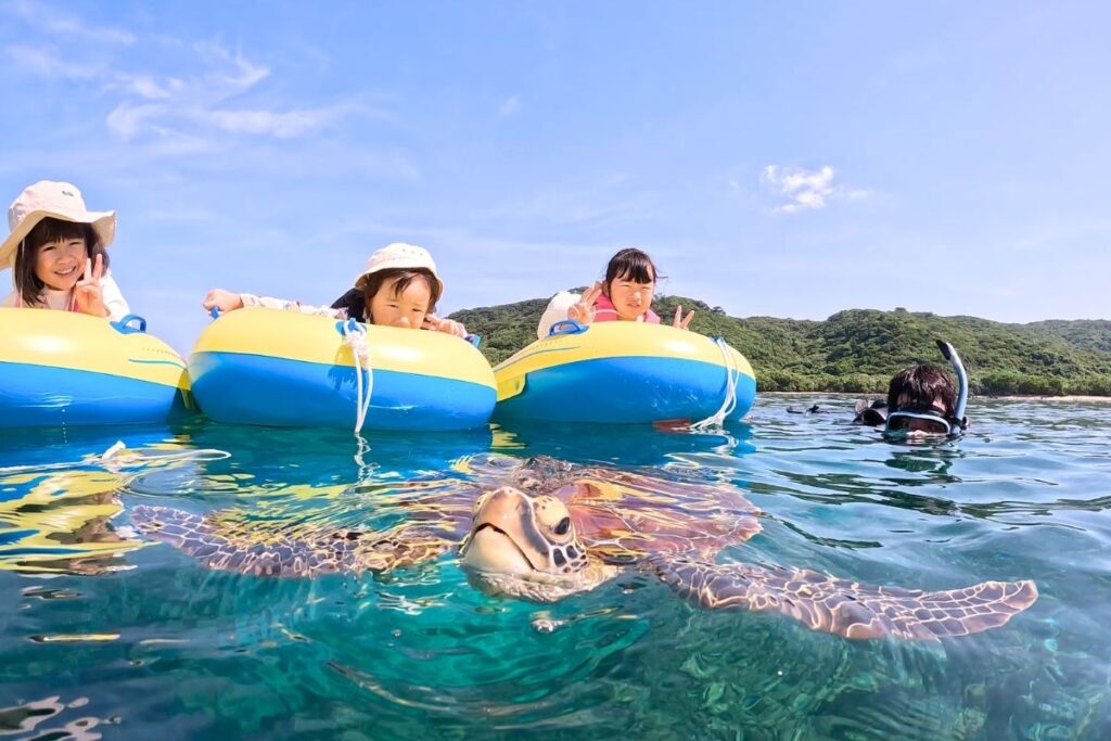 ぷかぷかと浮き輪チューブに乗る小さな子供たちの目の前で野生のウミガメがぷはっと息継ぎを見せてくれた瞬間の大興奮ショット
