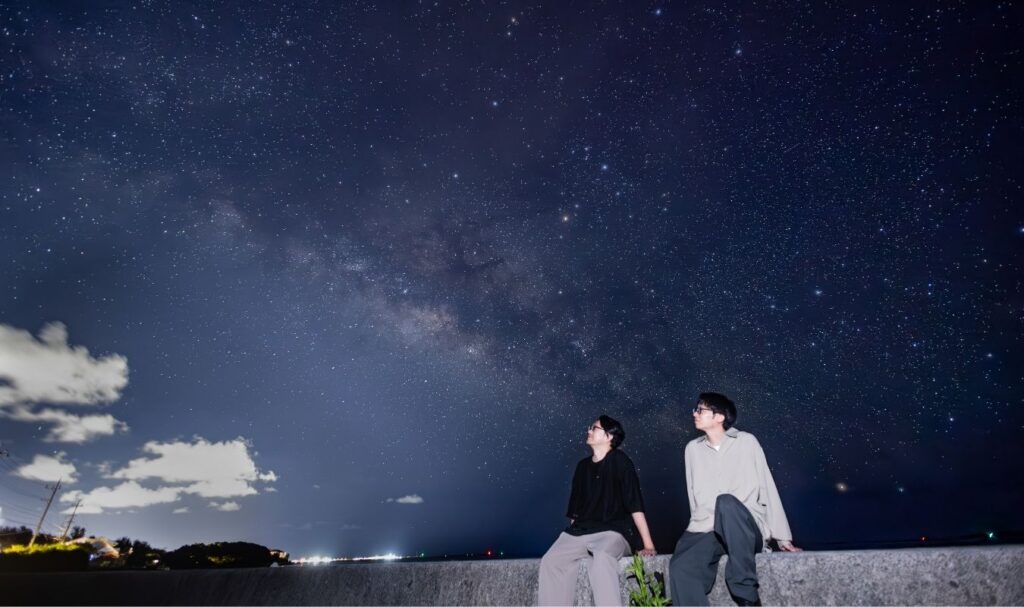 人工の光がない真っ暗な絶景スポットで並んで星空観測を楽しむ男性2人組のライフスタイル写真