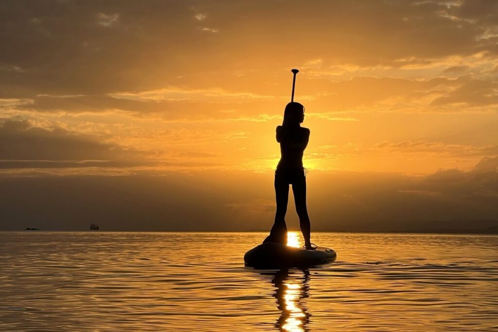 海面に伸びる黄金色の夕日の光の道（サンロード）を進む、石垣島サンセットSUPツアーでの女性参加者の美しい直立シルエット