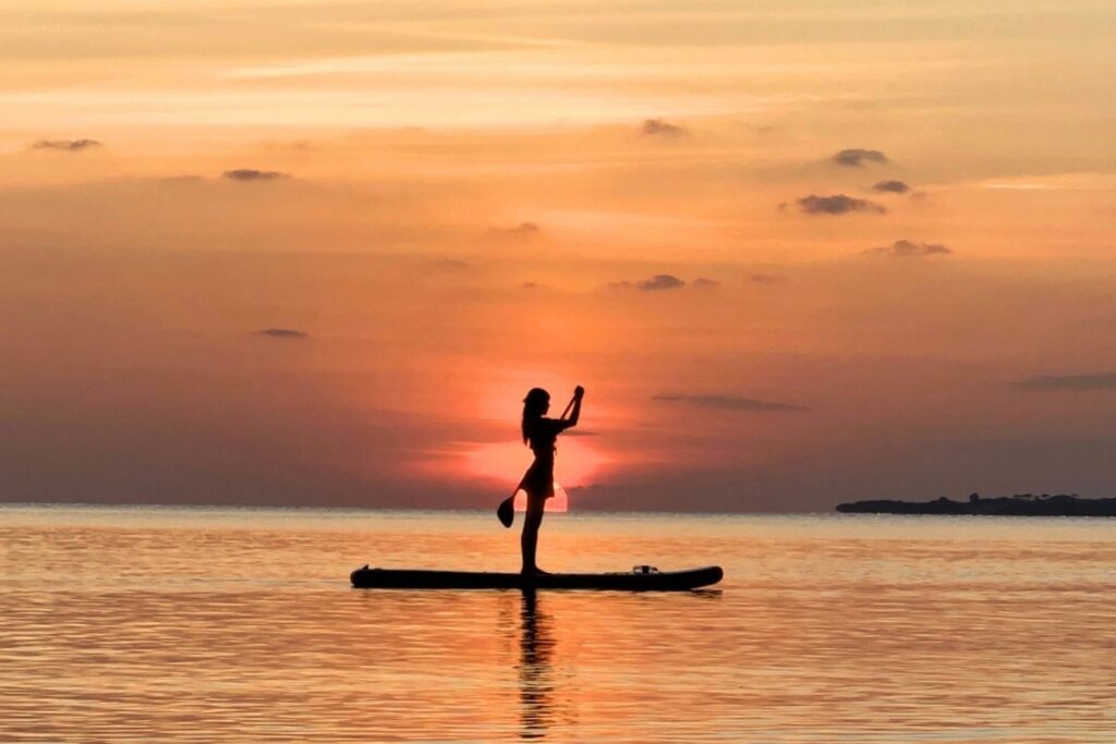 石垣島の黄金色に染まる海と夕日をバックに、サップボードの上に美しく直立する女性参加者の幻想的なシルエットフォト
