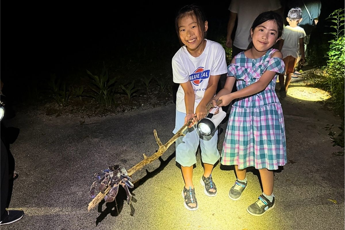石垣島の夜のジャングル探検ナイトツアーで大きなヤシガニを間近で観察して笑顔になる子どもたち RUANOA